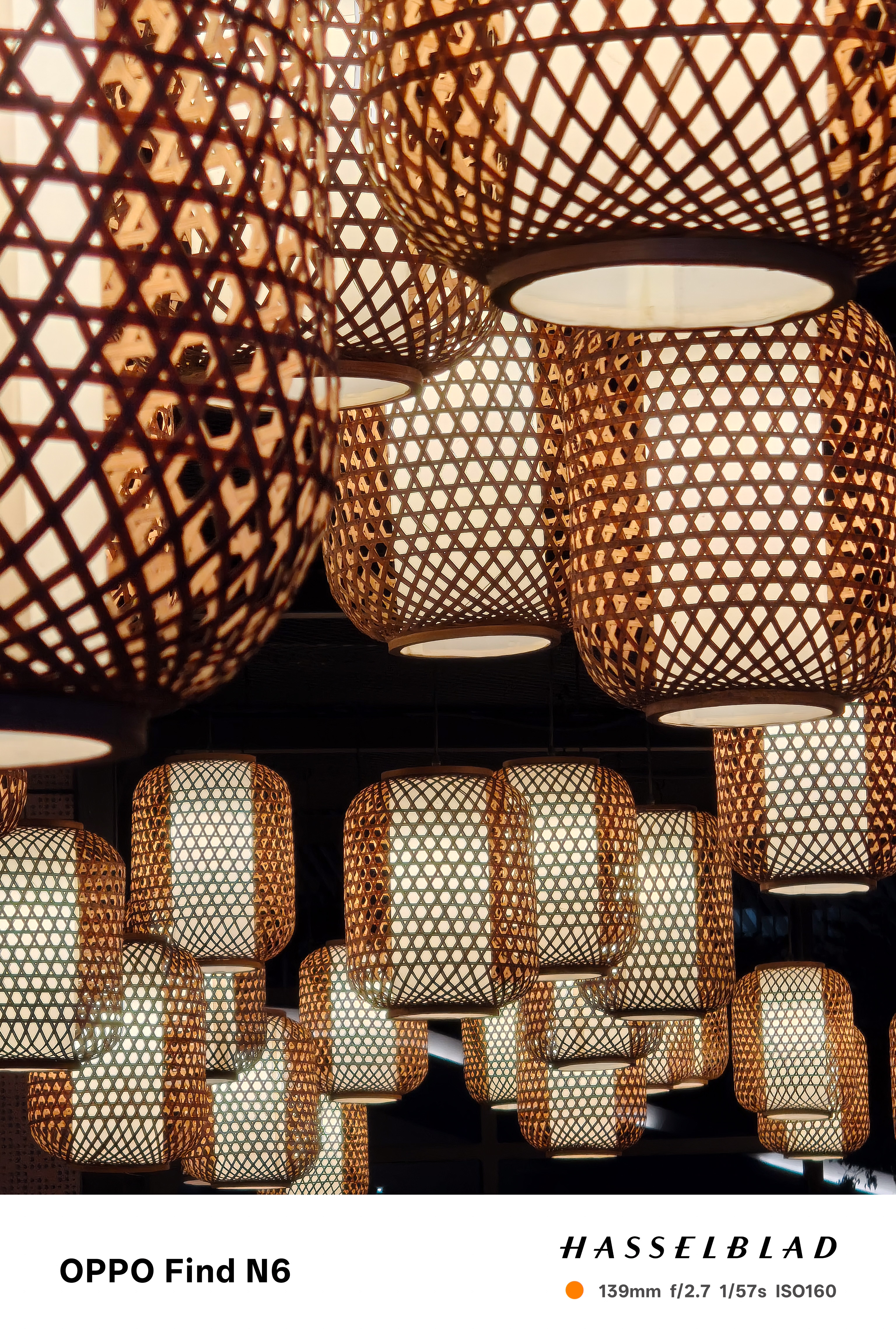 high-zoom telephoto shot capturing the intricate weave and warm glow of several hanging bamboo lanterns. The shallow depth of field creates a beautiful overlap of the patterns, highlighting the craftsmanship of the natural materials.