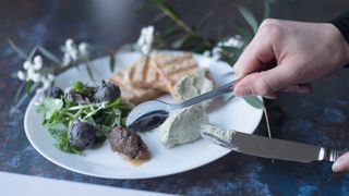 Hands holding a knife and spoon, arranging food on a plate