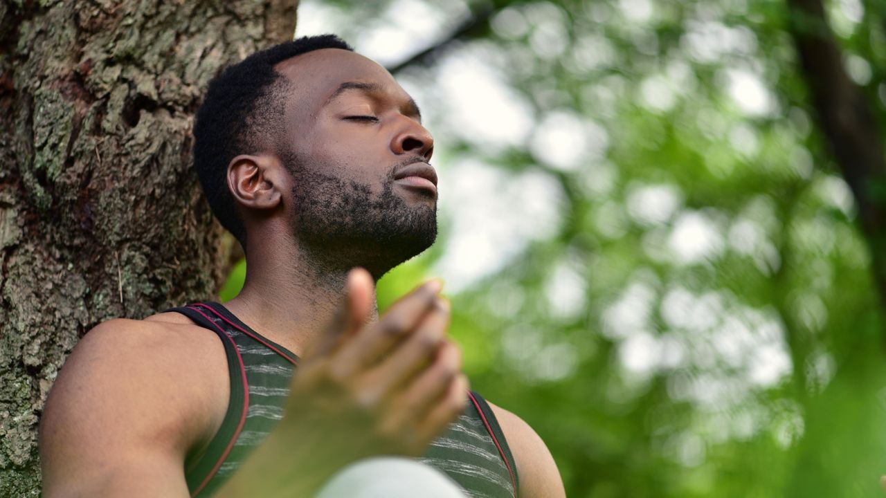 Man meditating outside near a tree