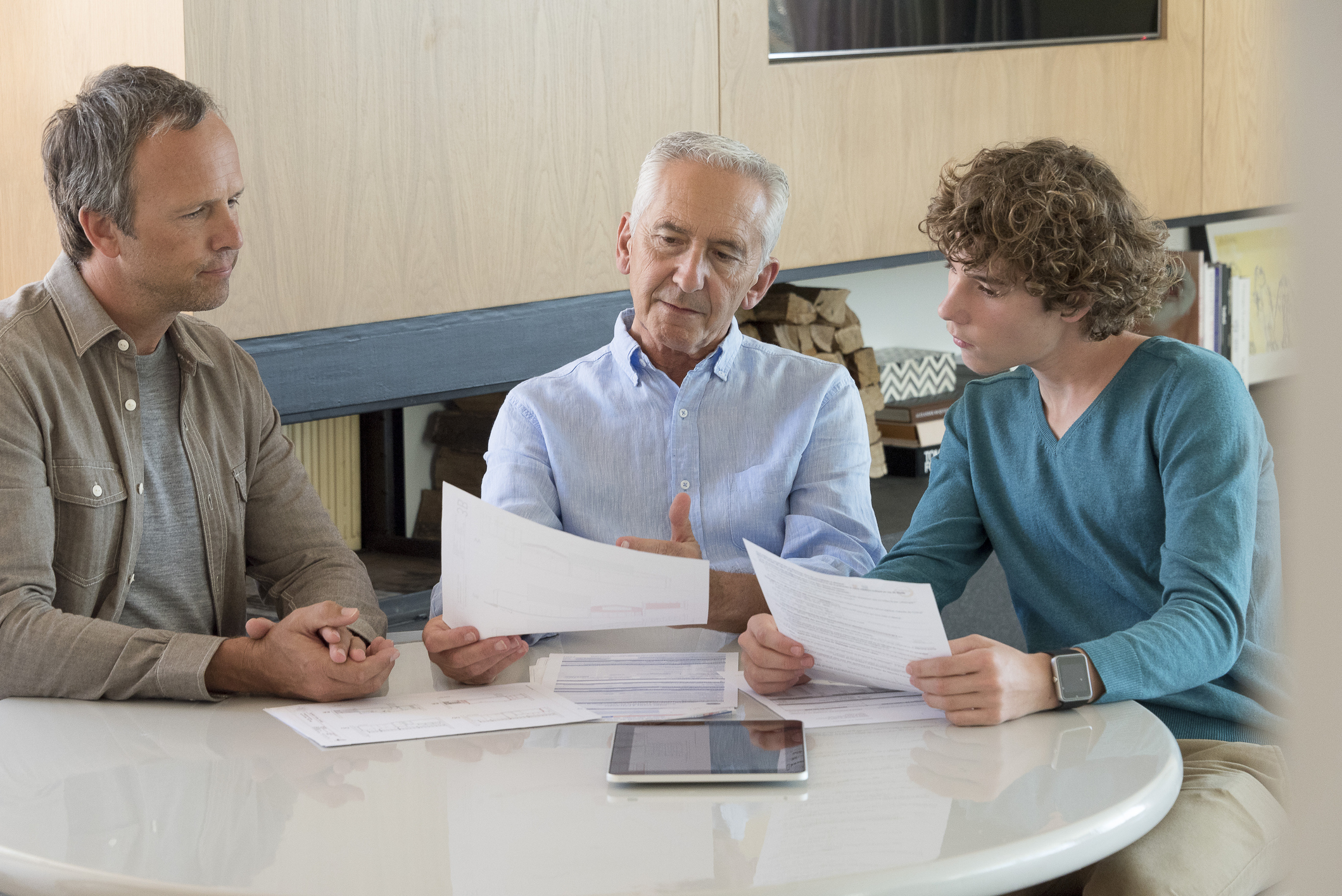 Senior man doing pension and inheritance planning with son and grandson in a living room