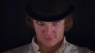 A man stares straight back at the camera, menacingly while wearing a black top hat, a white shirt and painted eyelashes underneath his right eye