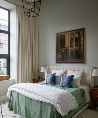 bedroom with light gray walls, green bedding and artwork above bed