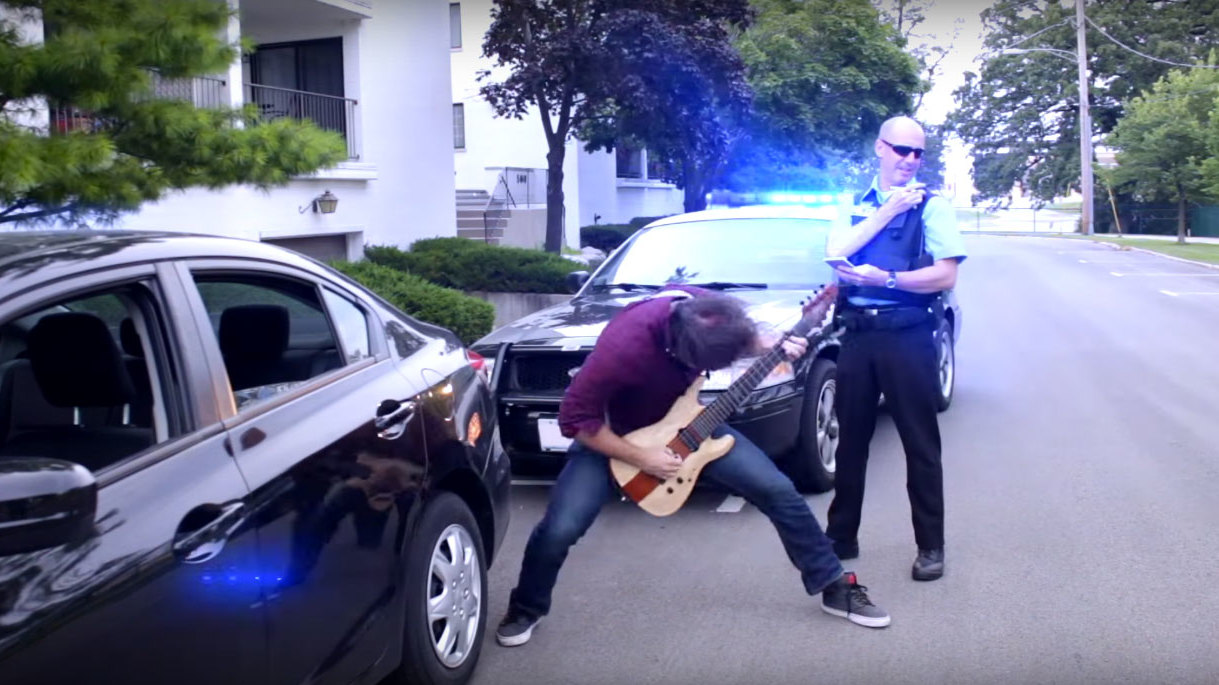 Rob Scallon playing guitar next to a police car