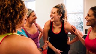 Group of female friends talking and laughing after a fitness class in the gym