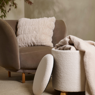 Boucle ottoman with blanket next to brown armchair with pink fluffy cushion