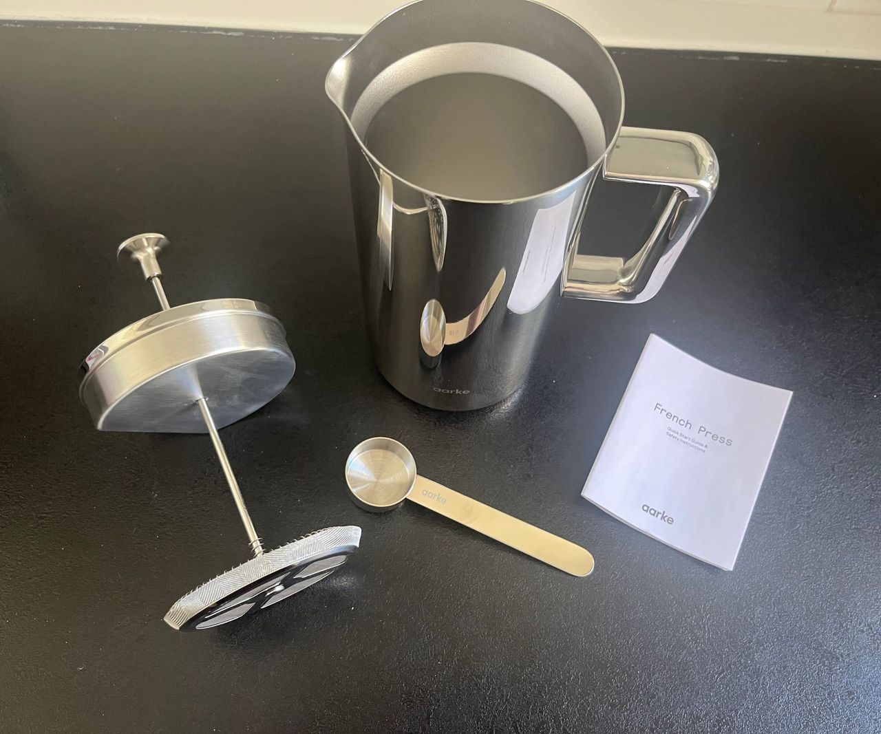 A stainless steel aarke coffee press with the plunger removed on a black counter