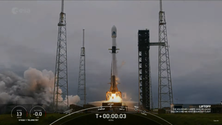 A white and black rocket launches into a cloudy sky.