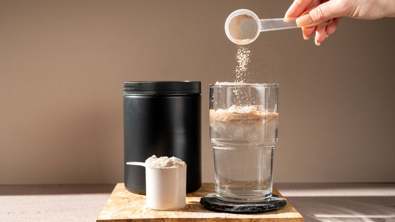 A person putting a scoop of protein powder into water