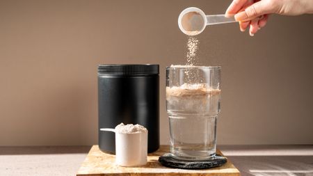 A person putting a scoop of protein powder into water