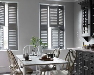 Kitchen with gray shutters on windows, rectangular wooden dining table with wooden dining chairs, gray kitchen units