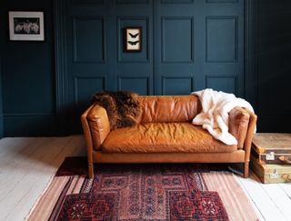A dark blue living room with a leather sofa and a boho pink rug.
