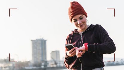 Woman looking at Fitbit and smartphone wearing activewear and warm hat outside, after finding out how to change the time on a Fitbit
