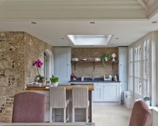 Interior of wraparound extension with kitchen with gray cabinets, breakfast bar and stools, and dining table and chairs in foreground