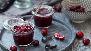 Cranberry sauce sitting in glass pot on stone tray with spoon