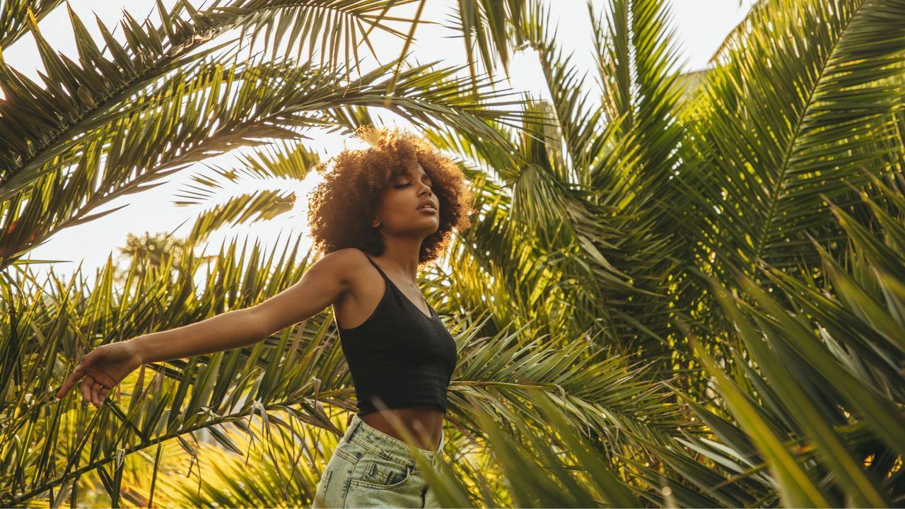 Woman with afro walking amongst palm trees in the sunshine