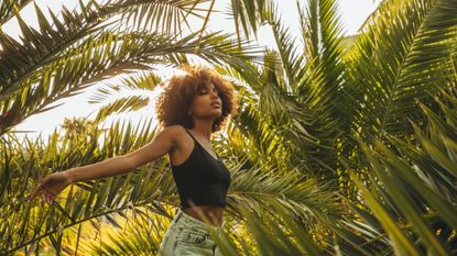 Woman with afro hair walking through palm trees in the sunshine