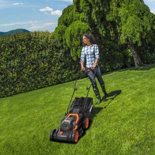 Worx WG779 cordless lawn mower being used by a woman on a large lawn