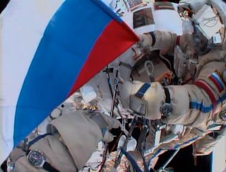 A cosmonaut holds a Russian flag during a spacewalk outside the International Space Station in honor of Russian Flag Day on Aug. 22, 2013.