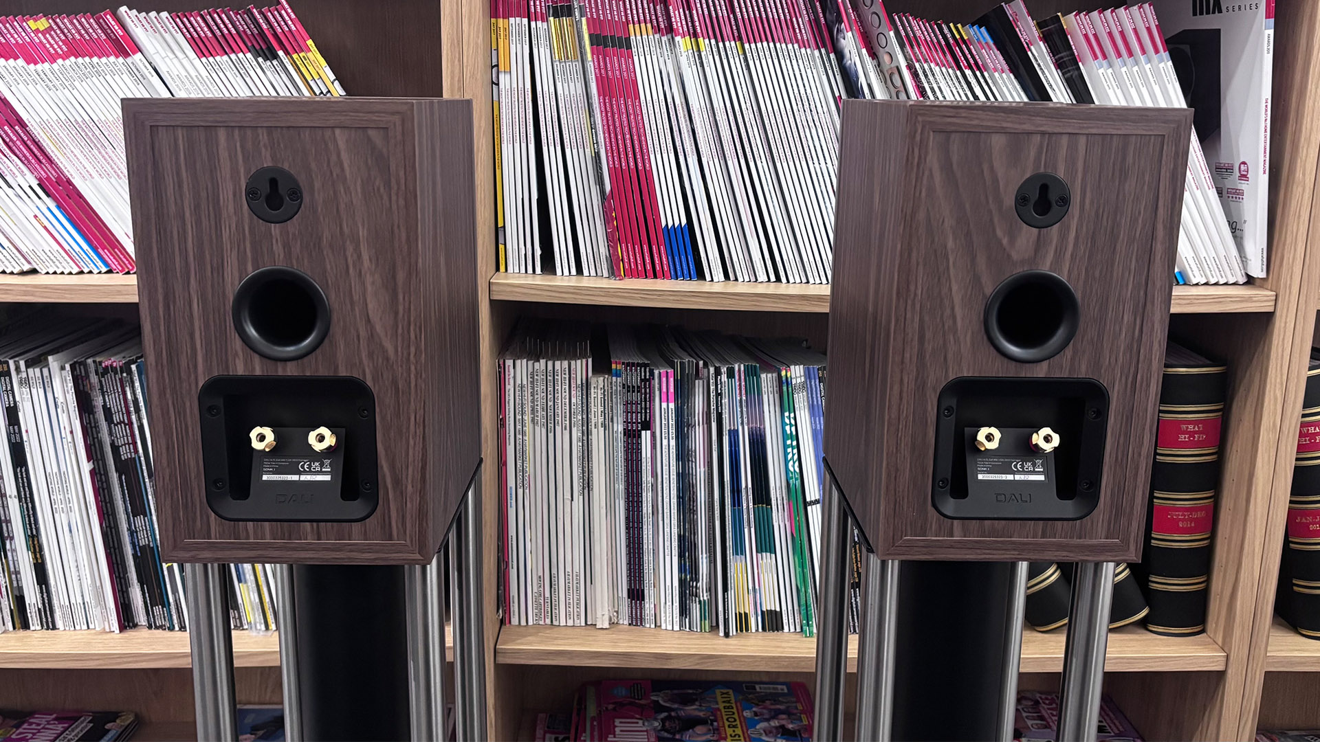 Dali Sonik 1 standmount speakers in front of bookcase, rear of speakers showing rear ports and binding posts