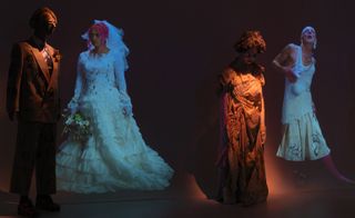 Alternative view of the Claire Barrow and Galeria Melissa installation featuring a mannequin in a suit next to a projected image of a person in a wedding dress and another mannequin in a dress next to a projected image of a person in a white outfit