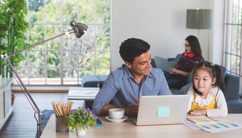 Father and daughter sit around computer on table