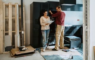 male and female couple stood in kitchen mid renovation looking at plans