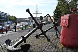 Two anchors displayed on a sidewalk next to a riverfront