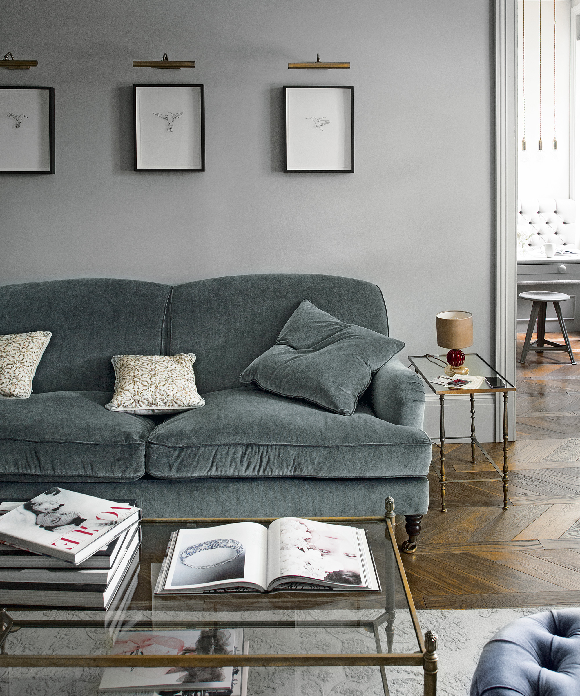 Grey living room ideas featuring a velvet grey sofa, pale grey walls and wooden flooring.