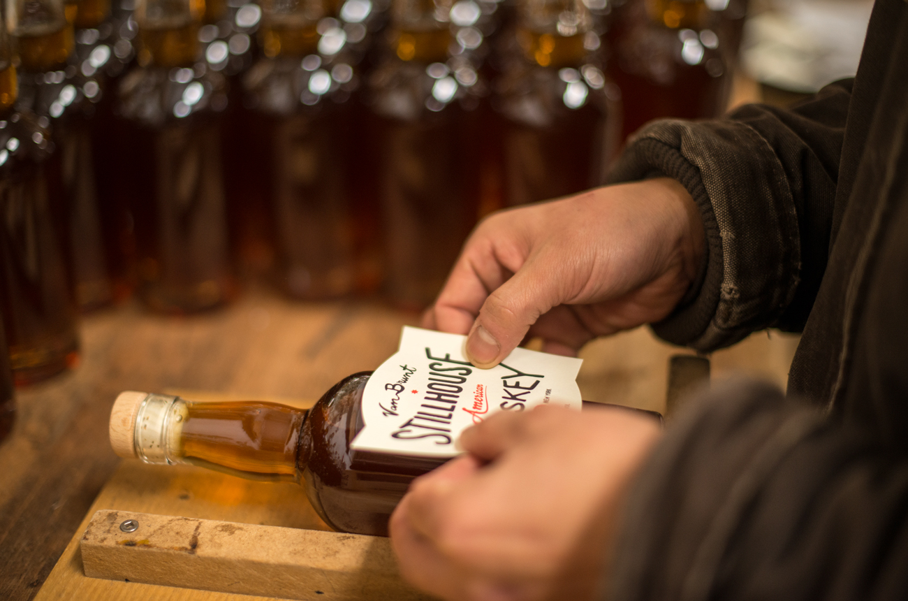 A close-up of a man's hands putting a label on a bottle of whiskey