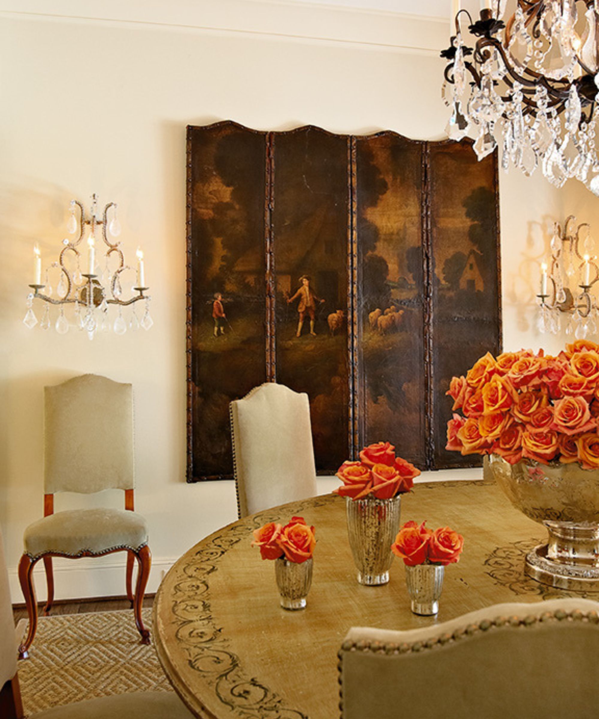 handpainted dining room table with antique wall decor and a large chandelier. the table is filled with fresh cut flowers