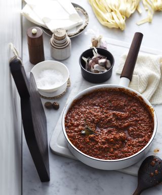 Bolognese ragu in pot with long-handled spoon and fresh egg pasta in background