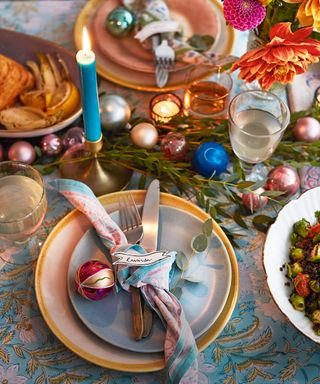 Overhead view of a table laid with colourful plates, Christmas baubles and lit candles. Festive table settings and cooked dishes at Christmas time