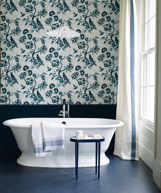 A bathroom with black wall panelling and flooring with patterned whimsical wallpaper