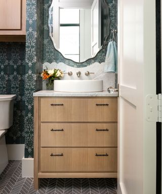 Small bathroom with teal wallpaper, wood vanity and wall unit, large mirror, marble splashback, grey floor tiles