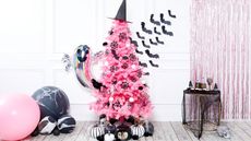 Pink Christmas tree decorated for Halloween using witches hat topper, adhesive bats on walls, silver foil ghost balloon, monochrome painted pumpkins