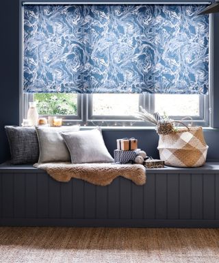 A blue window ledge with soft throws, pillows, and a basket