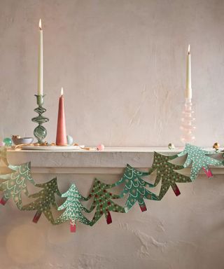 mantelpiece with white walls, green paper Christmas tree garland with tall taper candles on ledge