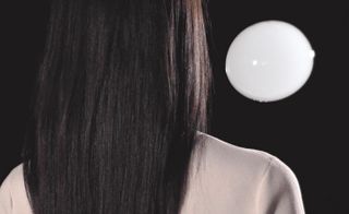 View of the back of a woman's head with long hair and a white bubble in a space with a black background