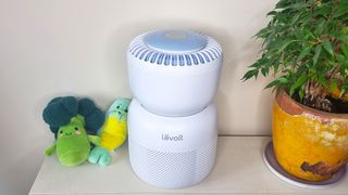 Levoit Sprout air purifier sat next to two plushie toys and a houseplant