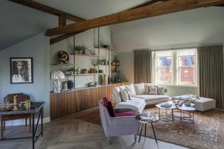 green living room with awkward shape walls, herringbone floor, vintage rug, shelving unit, artwork, drapes, side tables