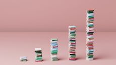 A digital image showing books stacked up in five increasingly large piles to resemble a graph. Decorative: the spines of the books are all different colours and they are set against a pink floor and wall.