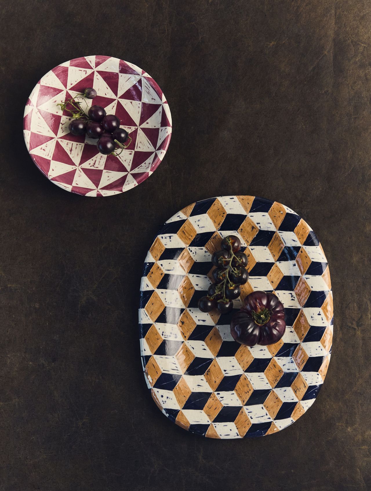 Two geometric printed ceramic dishes on a dark wood table.