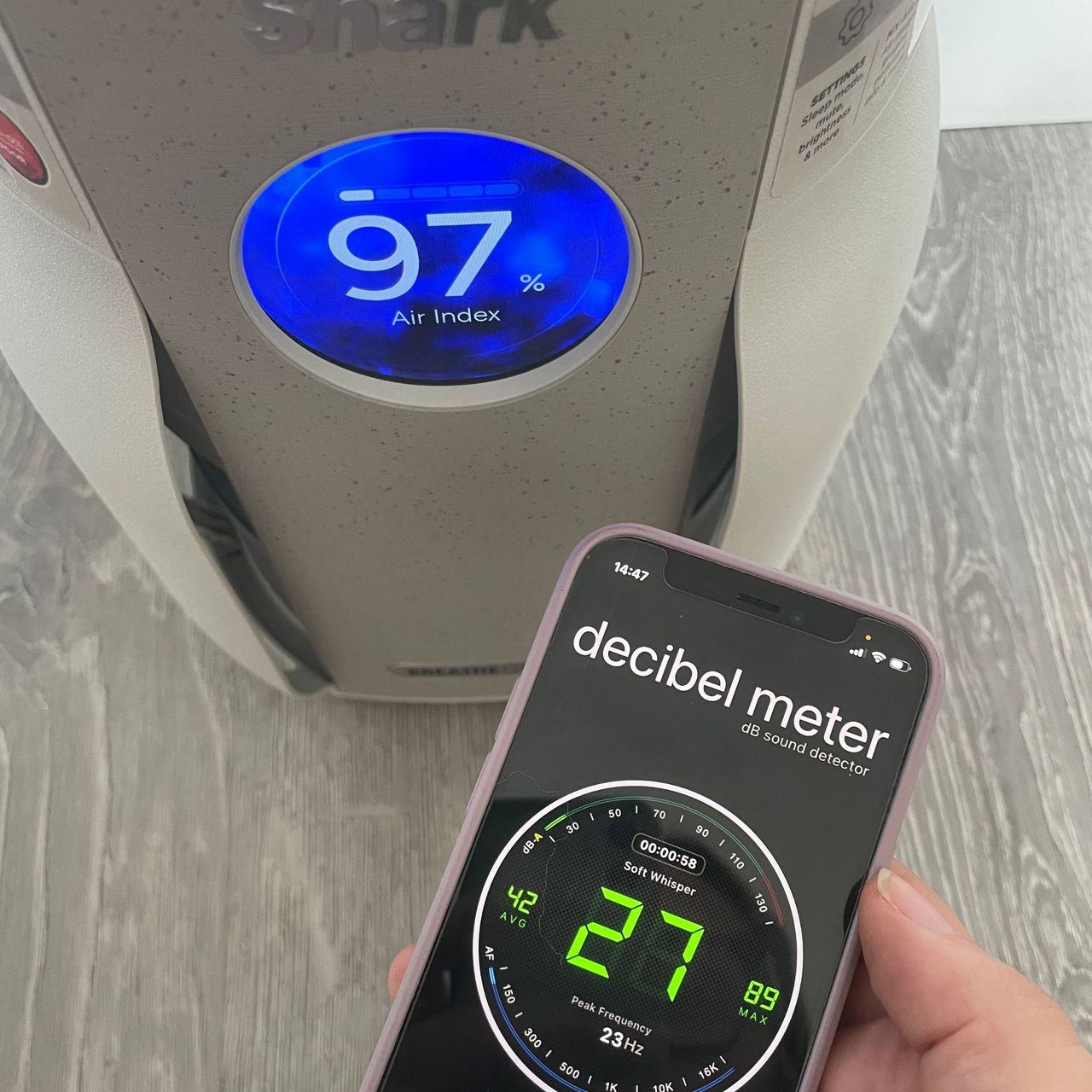 decibel meter app sitting next to a shark air purifier, showing a reading of 27 decibels