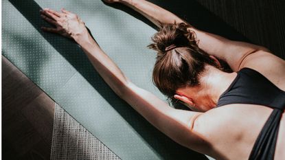 Woman stretching out on yoga mat doing Pilates for beginners in the sun