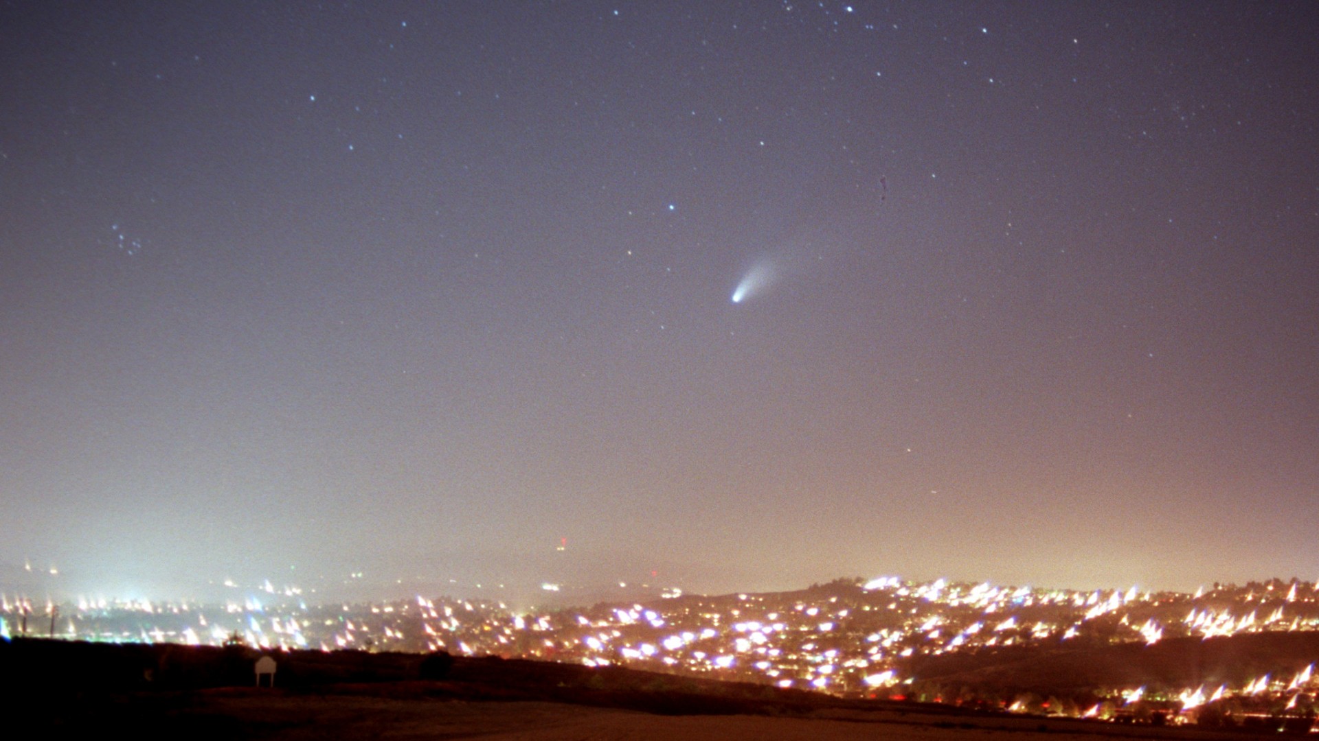 Ein heller Komet über einem hellen Feld aus Stadtlichtern