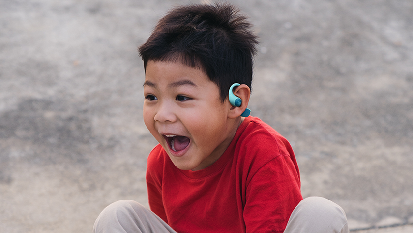 JBL Junior Free headphones worn by a child who is yelling in happiness. The earbuds are hooked around his ears