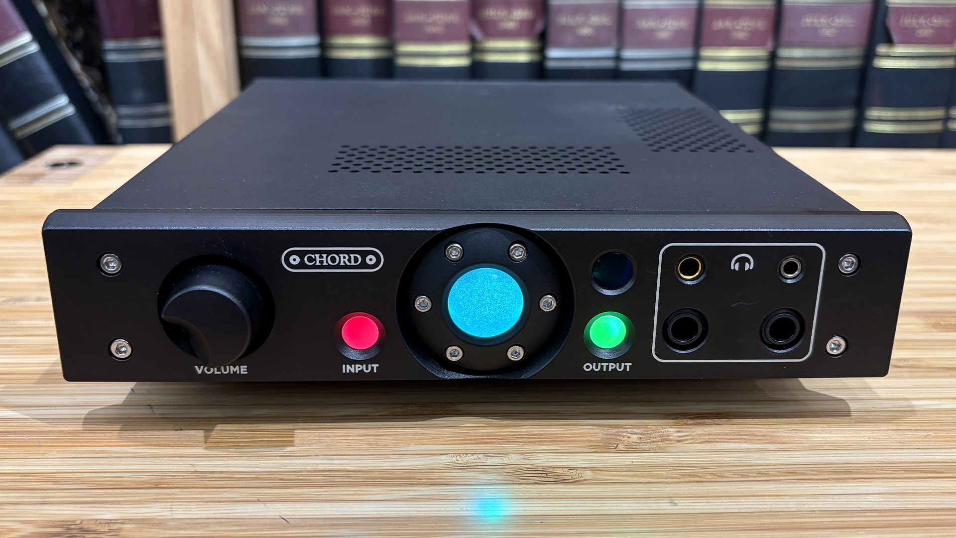 Chord Electronics Alto headphone amp on wooden surface in front of bookcase