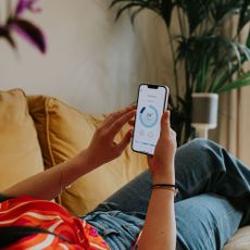 Energy-saving tech close up of a person lying on a sofa using a mobile phone to control a smart thermostat