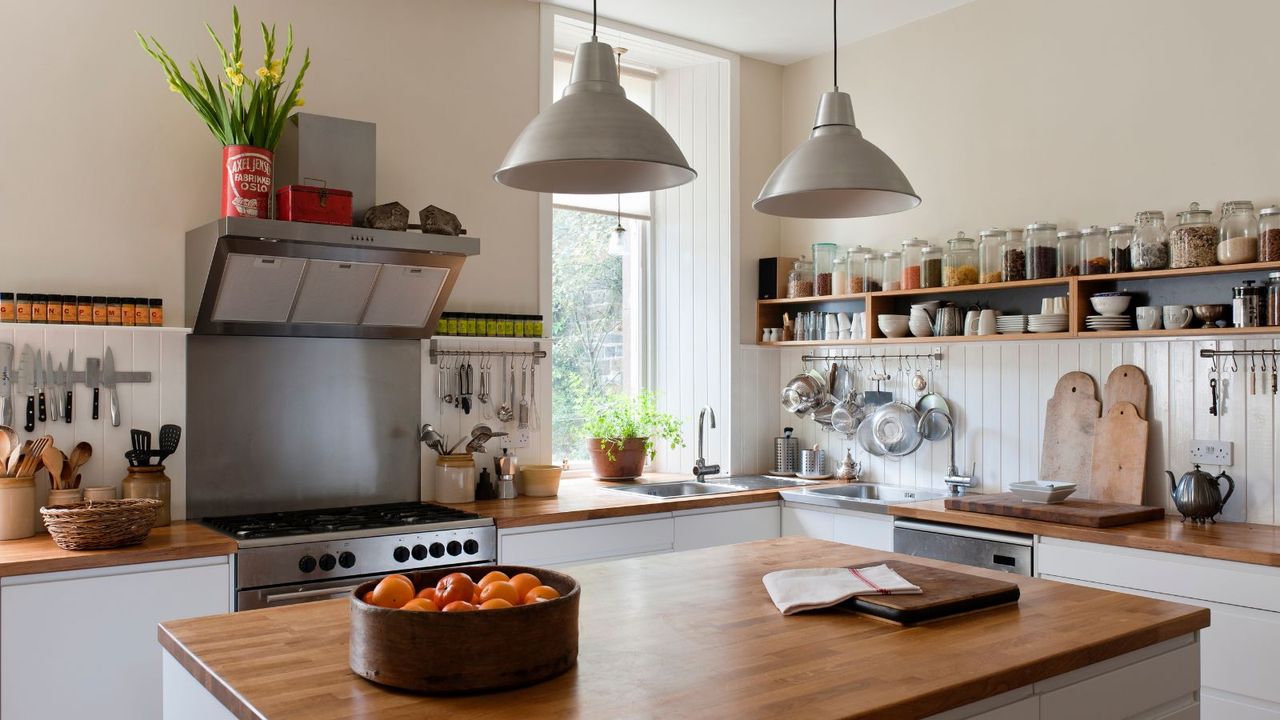 Country style kitchen with white cabinets, vertically paneled walls with open shelving, wooden counters and a large kitchen island