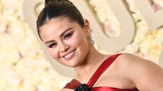 Selena Gomez wearing a strappy red silk dress with her brown hair in an up-do, with a white floral background behind her